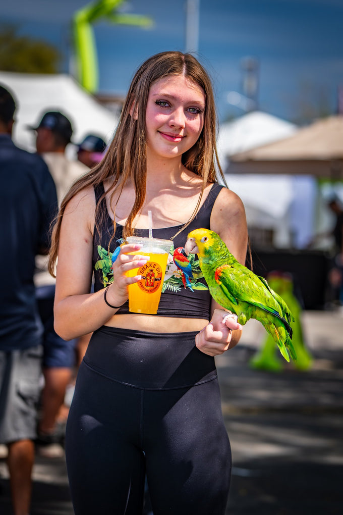 Woman holding a ready-to-drink Elysian Orange with a parrot on her arm in an outdoor setting