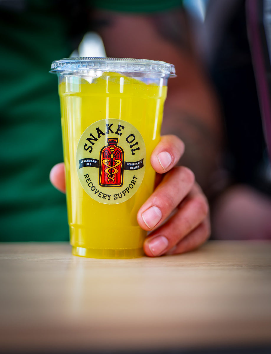 A hand holding a Ginger Bite recovery drink with the Snake Oil logo facing forward